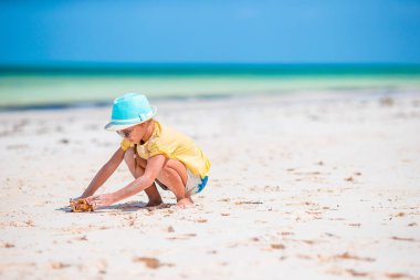 Tropik beyaz sahildeki küçük kız kumdan kale yapıyor.