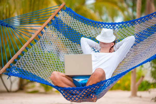 Jongeman met laptop bij hangmat op tropische vakantie — Stockfoto