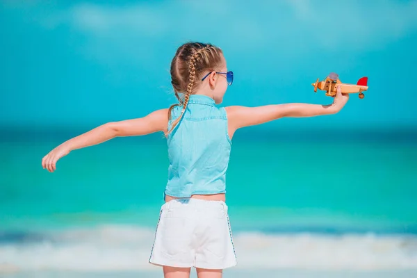 Happy little girl with toy airplane in hands on white sandy beach. — Stock Photo, Image