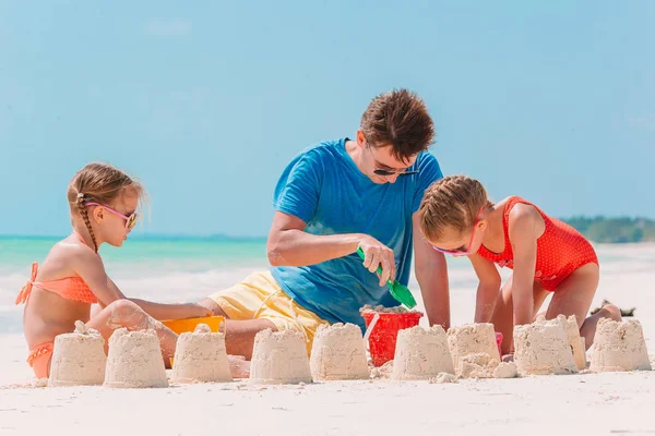 Vader en kinderen maken zandkasteel op tropisch strand. Familie spelen met strand speelgoed — Stockfoto