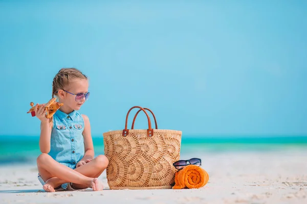 Happy little girl with toy airplane in hands on white sandy beach. — Stock Photo, Image