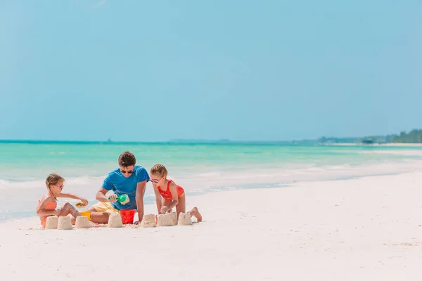 Ojciec i dzieci robią zamek z piasku na tropikalnej plaży. Zabawa rodzinna zabawkami plażowymi — Zdjęcie stockowe