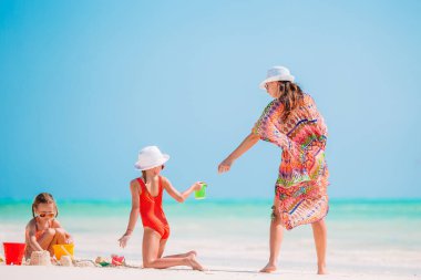 Anne ve küçük kızları tropik sahilde kumdan kale yapıyorlar.