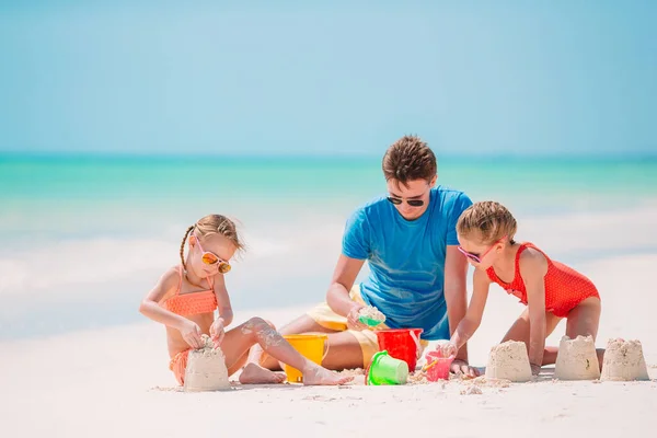 Ojciec i dzieci robią zamek z piasku na tropikalnej plaży. Zabawa rodzinna zabawkami plażowymi — Zdjęcie stockowe