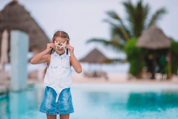 Adorable little girl with starfish on white empty beach — Stock Photo, Image