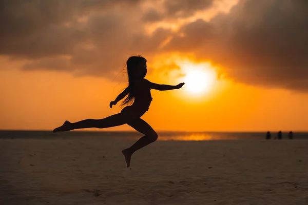 Αξιολάτρευτο χαρούμενο κοριτσάκι σε λευκή παραλία το ηλιοβασίλεμα. — Φωτογραφία Αρχείου