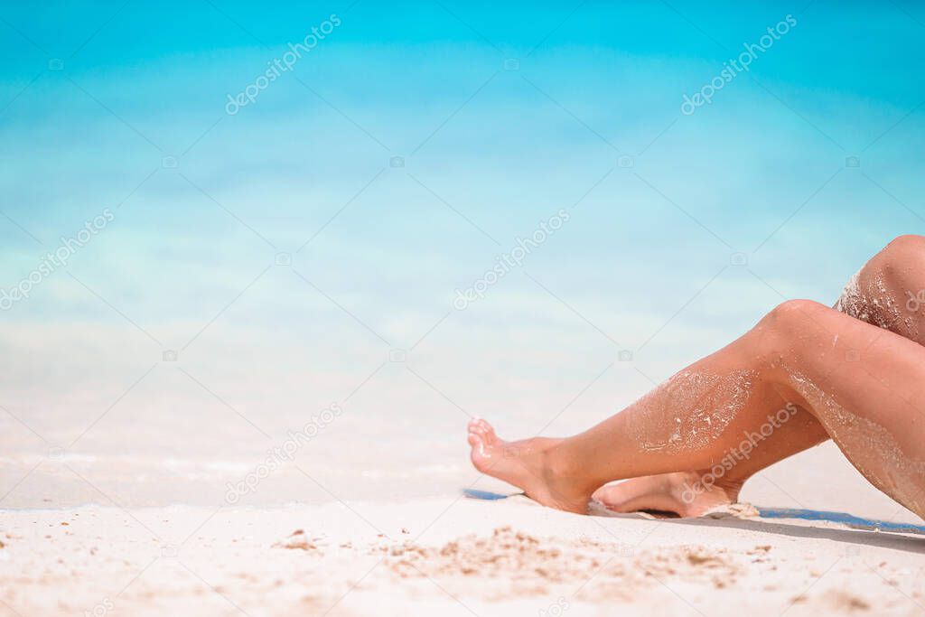 Womans feet on the white sand beach in shallow water