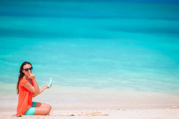 Tropikal plajda elinde güneş kremi tutan güzel genç bir kadın. — Stok fotoğraf
