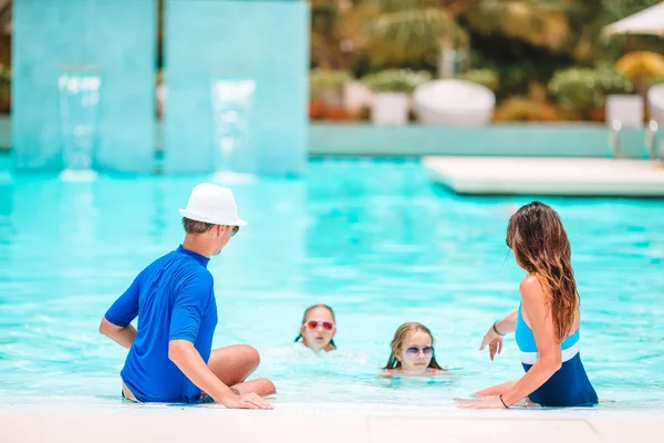 Familia joven con dos niños disfrutan de vacaciones de verano en la piscina al aire libre — Foto de Stock