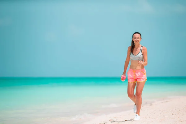 Spor kıyafetleriyle tropikal beyaz plajda egzersiz yapan zinde genç bir kadın. — Stok fotoğraf
