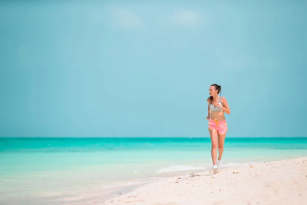 Fit young woman doing exercises on tropical white beach in her sportswear — Stock Photo, Image