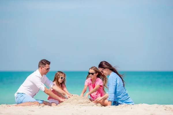 Familia de cuatro haciendo castillo de arena en la playa tropical blanca —  Fotos de Stock