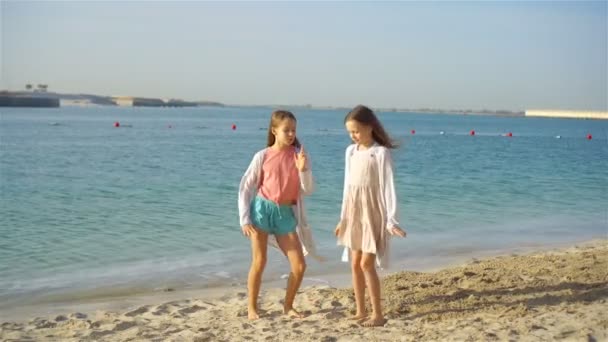 Pequenas meninas engraçadas felizes se divertir muito na praia tropical jogando juntos. Dia ensolarado com chuva no mar — Vídeo de Stock