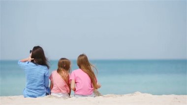 Anne ve küçük kızları tropik sahilde kumdan kale yapıyorlar.