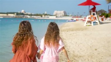 Küçük mutlu komik kızlar tropikal plajda birlikte oynarken çok eğleniyorlar. Denizde yağmurlu güneşli bir gün