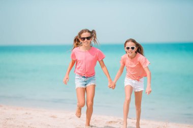 Küçük mutlu komik kızlar tropikal plajda birlikte oynarken çok eğlenirler..