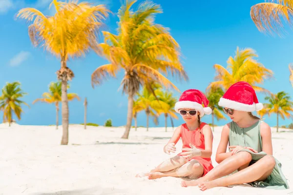 Kleine schattige meisjes in Santa hoeden tijdens strandvakantie hebben plezier samen — Stockfoto