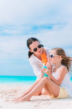 Genç anne sahildeki kızına güneş kremi sürüyor. Güneş koruması