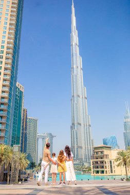 Arka planda gökdelenlerle Dubai 'de yürüyen mutlu bir aile..