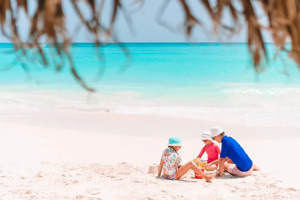 Ojciec i dzieci robią zamek z piasku na tropikalnej plaży. Zabawa rodzinna zabawkami plażowymi — Zdjęcie stockowe