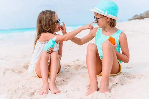 Tropikal plajda oturan güneş kremi şişeli küçük kız. — Stok fotoğraf