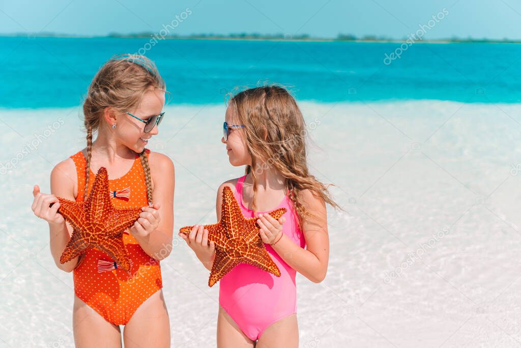 Adorable little girls with starfish on white empty beach