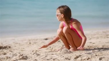 Tropik beyaz sahildeki küçük kız kumdan kale yapıyor.