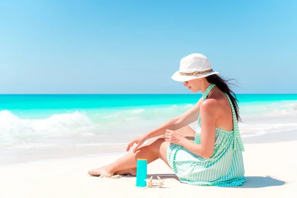 Beautiful young woman holding a suncream lying on beach — Stock Photo, Image