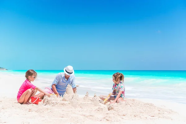 Otec a malé dcery, takže hrad z písku na tropické pláži — Stock fotografie
