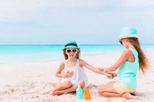 Tropikal plajda oturan güneş kremi şişeli küçük kız. — Stok fotoğraf