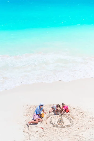 Pai e filhas fazendo castelo de areia na praia tropical — Fotografia de Stock