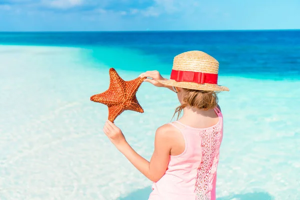 Adorable little girl with starfish on white empty beach — Stock Photo, Image