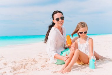 Genç anne sahildeki kızına güneş kremi sürüyor. Güneş koruması