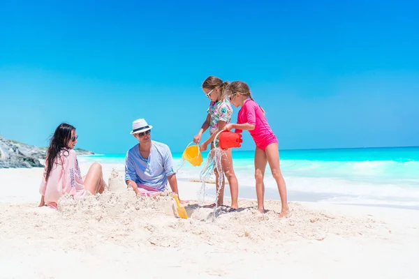 Familie van vier maken zandkasteel op tropisch wit strand — Stockfoto