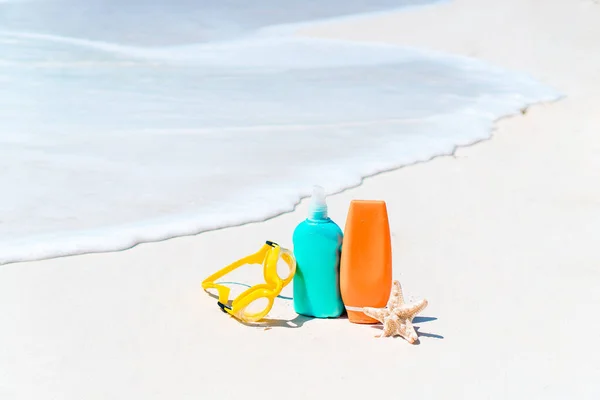 Suncream bottles, goggles, starfish and sunglasses on white sand beach background ocean — Stock Photo, Image