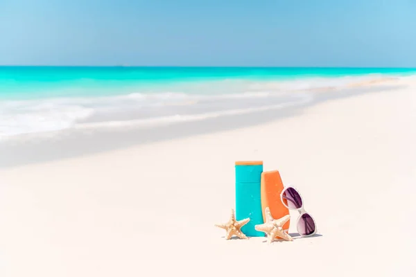 Suncream bottles, goggles, starfish and sunglasses on white sand beach background ocean — Stock Photo, Image