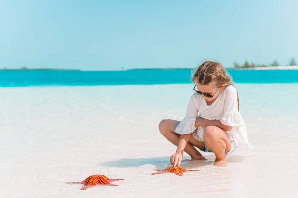 Adorable little girl with starfish on white empty beach — Stock Photo, Image