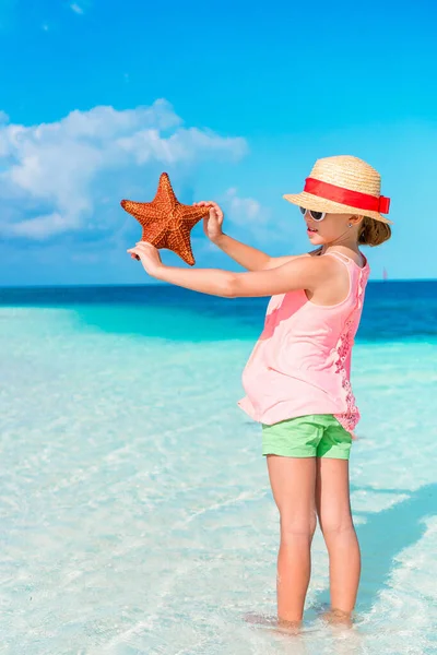 Schattig klein meisje met zeester op wit leeg strand — Stockfoto