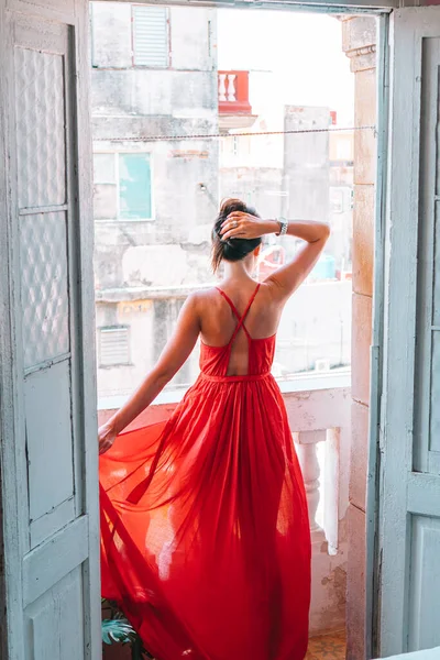 Νεαρή ελκυστική γυναίκα με κόκκινο φόρεμα στο παλιό μπαλκόνι στο διαμέρισμα στην Αβάνα — Φωτογραφία Αρχείου