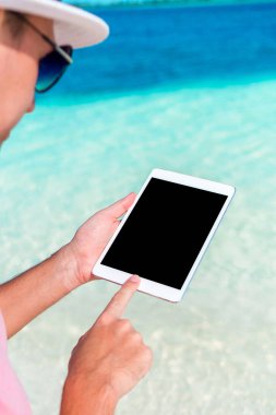 Adam plajda oturup tablet bilgisayarla çalışıyor.