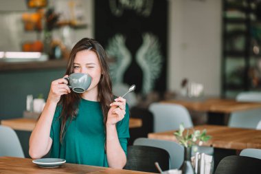 Güzel, zarif bir kız açık kafede kahvaltı yapıyor..
