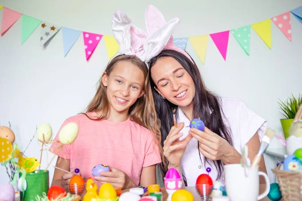 Mutter und ihre kleine Tochter bemalen Eier. Glückliche Familie bereitet sich auf Ostern vor. — Stockfoto