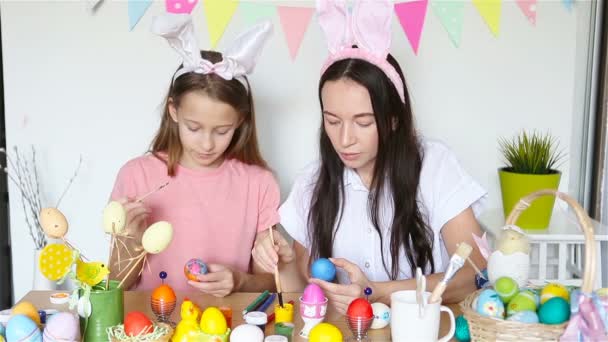 Madre y su pequeña hija pintando huevos. Familia feliz preparándose para la Pascua. — Vídeos de Stock