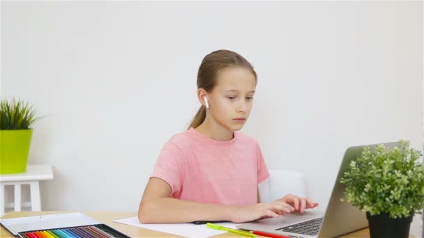 Colegiala seria sentada en la mesa con portátil y libro de texto y haciendo la tarea . — Vídeo de stock