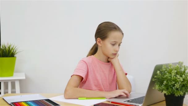 Colegiala seria sentada en la mesa con portátil y libro de texto y haciendo la tarea. Estudio desde casa — Vídeos de Stock