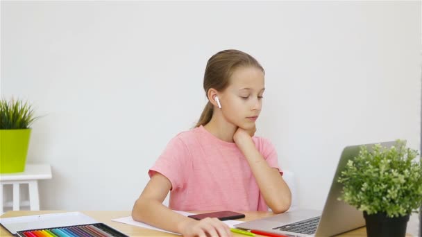 Colegiala seria sentada en la mesa con portátil y libro de texto y haciendo la tarea. Estudio desde casa — Vídeo de stock