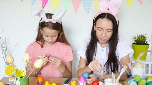 Madre y su pequeña hija pintando huevos. Familia feliz preparándose para la Pascua. — Vídeos de Stock