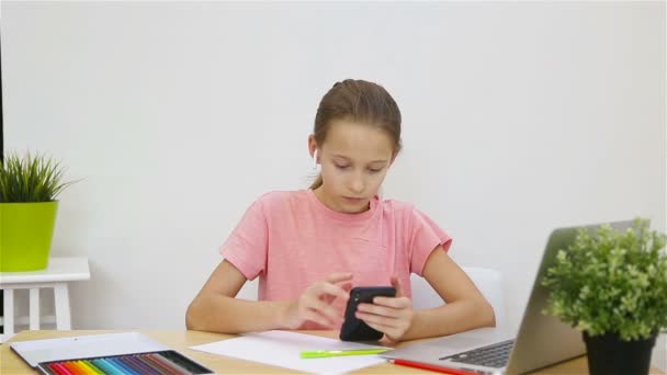 Serious schoolgirl sitting at table with laptop and textbook and doing homework. Study from home — Stock Video