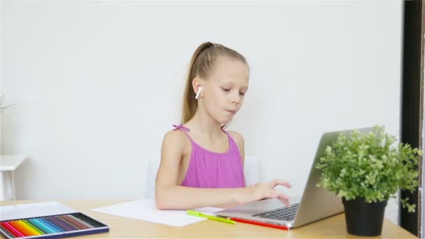 Seriös skolflicka sitter vid bordet med bärbar dator och lärobok och gör läxor. — Stockvideo