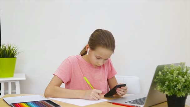 Seriös skolflicka sitter vid bordet med laptop och lärobok och gör läxor. Studie hemifrån — Stockvideo